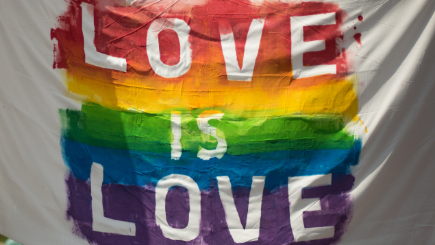 Bandeira arco-íris com a frase 'Love is Love' escrita no meio