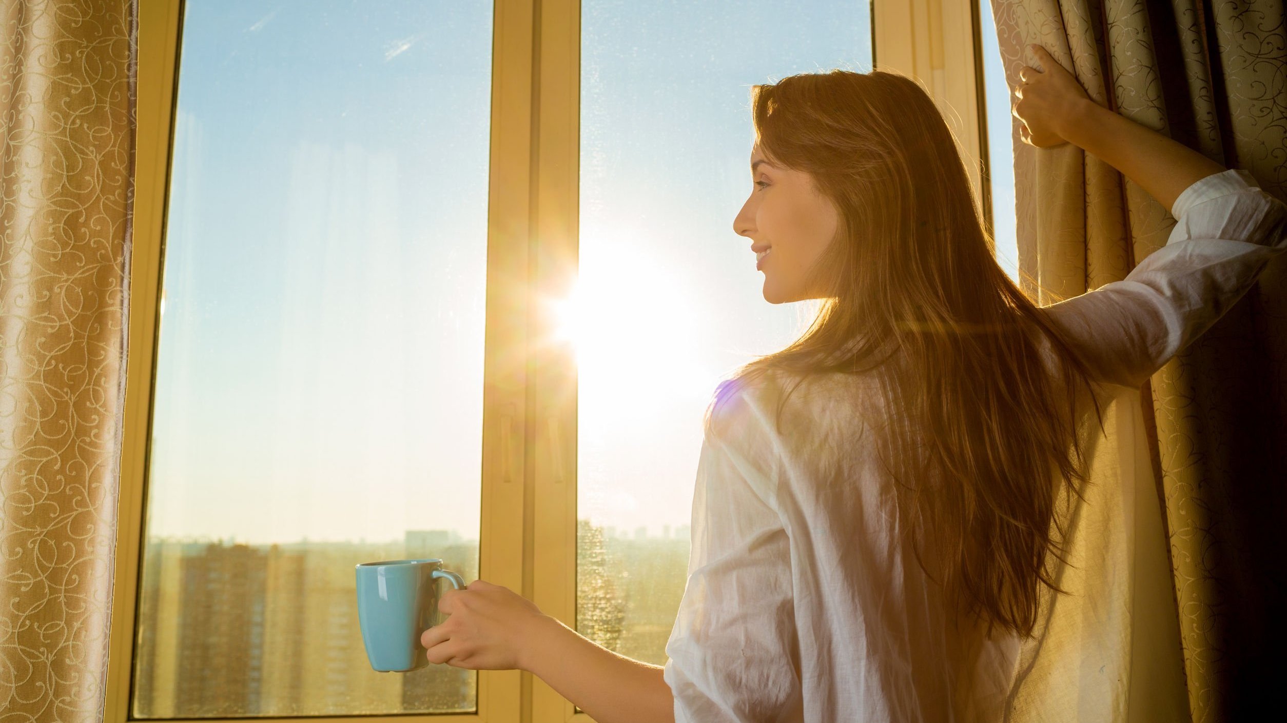 Mulher de costas abrindo a janela com sol refletindo