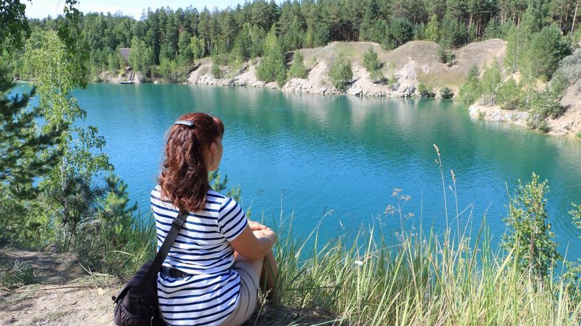 Mulher sozinha, sentada a beira de um lago, durante o dia.
