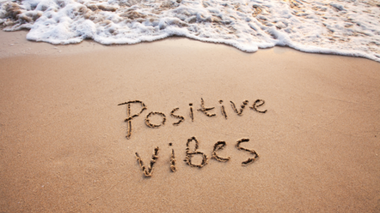 'Positive vibes' escrito na areia da praia com uma onda atrás