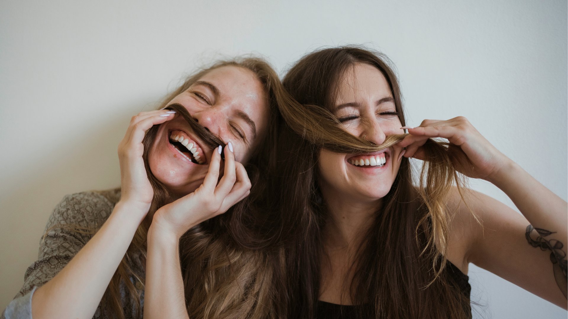 Duas amigas brincando com o cabelo da outra e sorrindo