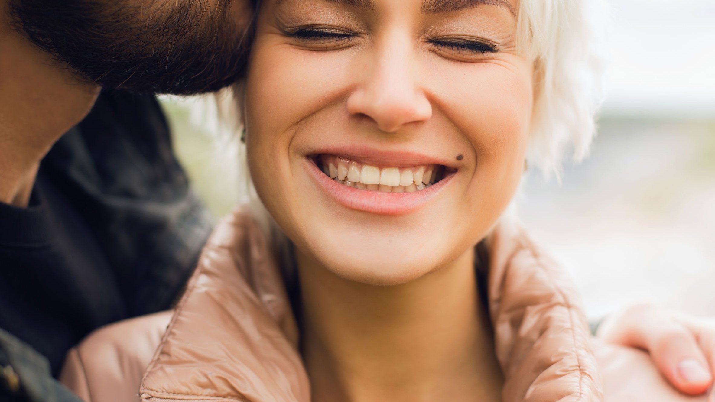 Homem beijando a cabeça da mulher que está com os olhos fechados e sorrindo