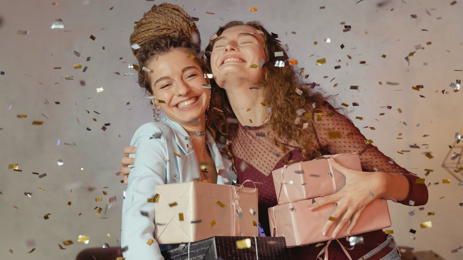 Duas mulheres se abraçando com presentes na mão e confetes caindo sobre elas