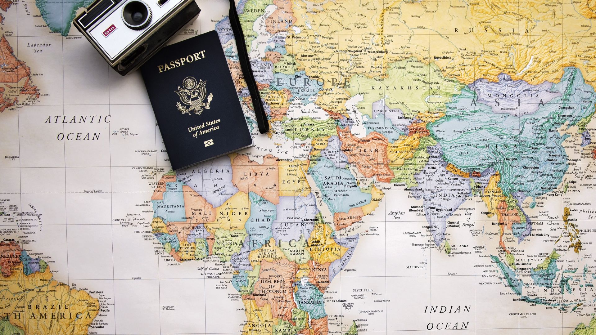 Imagem do mapa do mundo. Sobre ele, um passaporte e uma câmera fotográfica antiga.