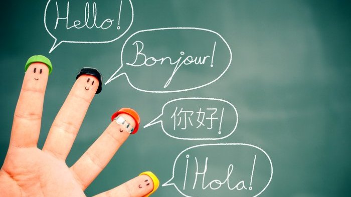 Quatro dedos fantasiados com carinhas e chapéus. Atrás deles, uma lousa na qual está escrito oi em inglês, francês, chinês e espanhol.