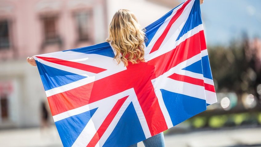 Jovem branca de costas estendendo bandeira do Reino Unido.