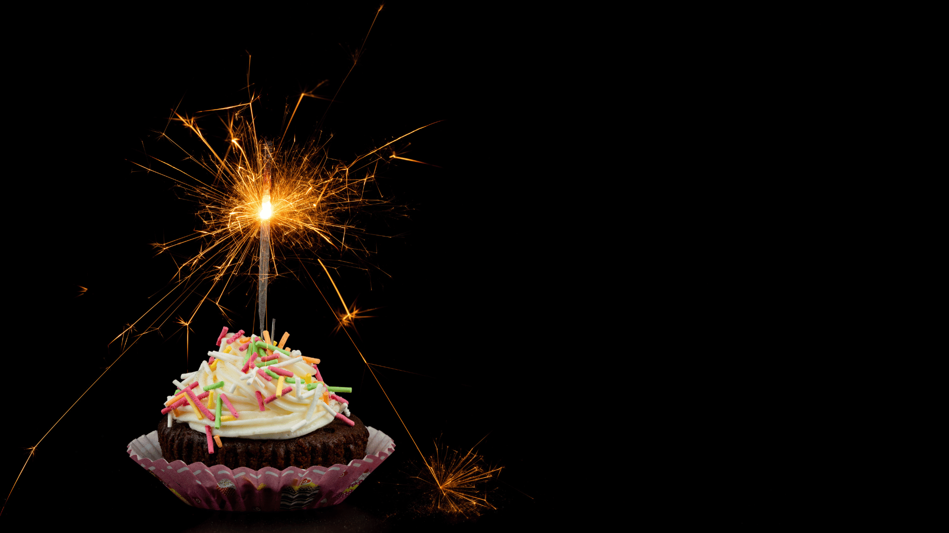 Um cupcake com uma vela artifício em fundo preto.