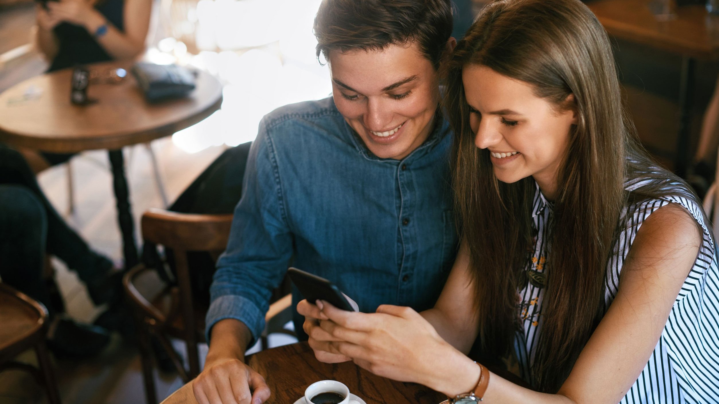 Homem e mulher em uma cafeteria olhando para o celular e sorrindo