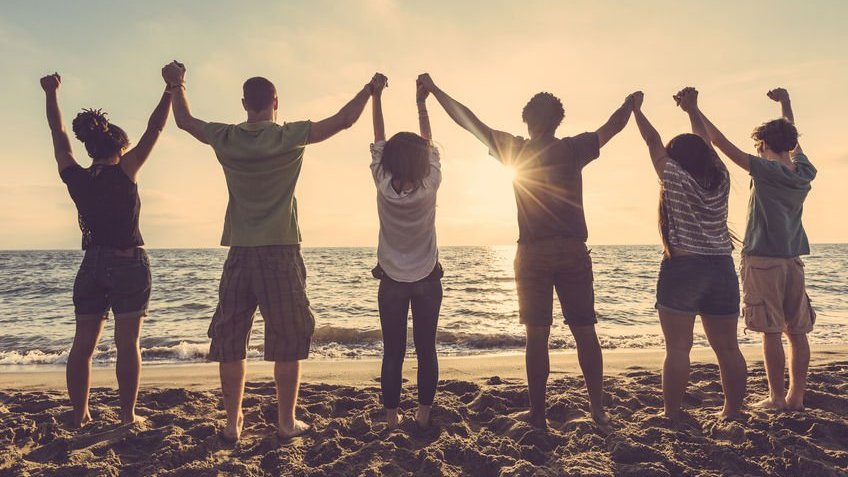Grupo de amigos vendo o pôr do sol e dando as mãos na praia
