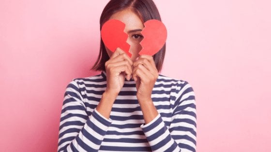 Menina com blusa listrada segurando um coração quebrado ao meio com o fundo rosa