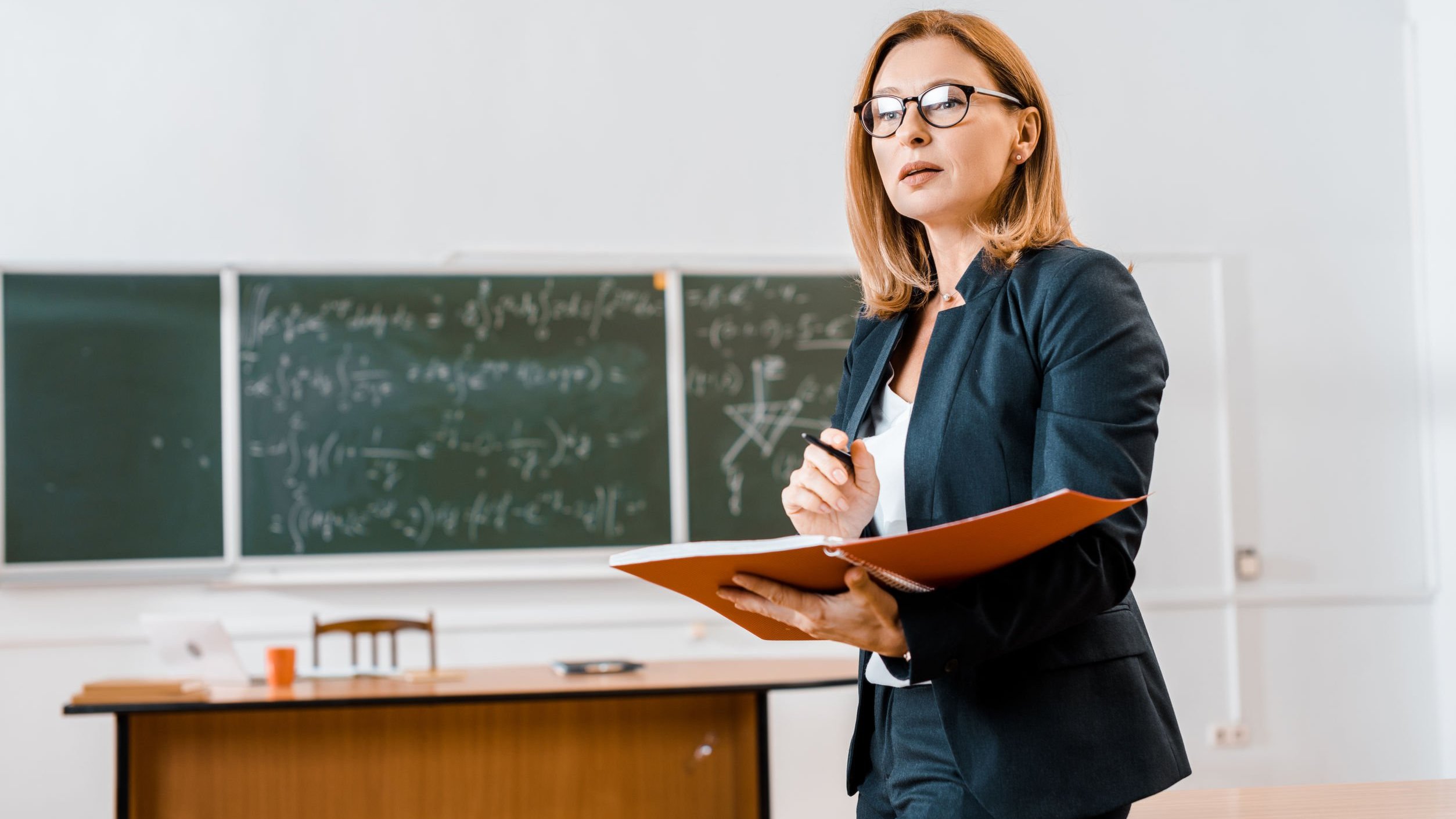 Professora em sala de aula segurando um caderno e caneta