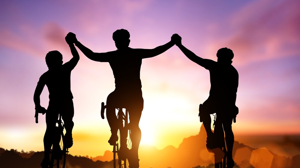 3 amigos segurando as mãos no alto enquanto dirigem uma bicicleta