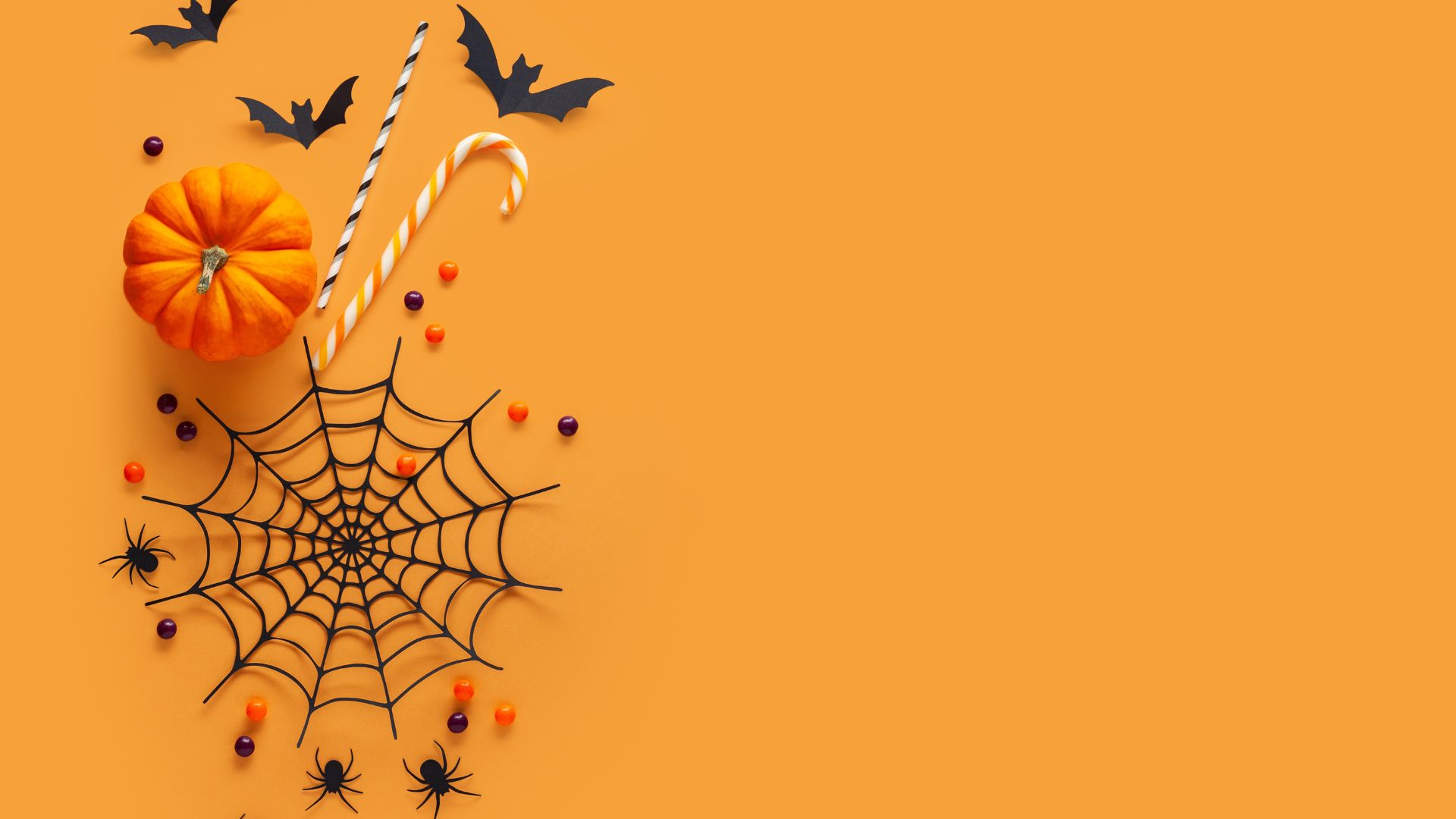 Imagem de fundo alaranjado. Ao lado esquerdo da tela, ícones que simbolizam o halloween como: abóbora, morcegos, aranhas e teias de aranhas.