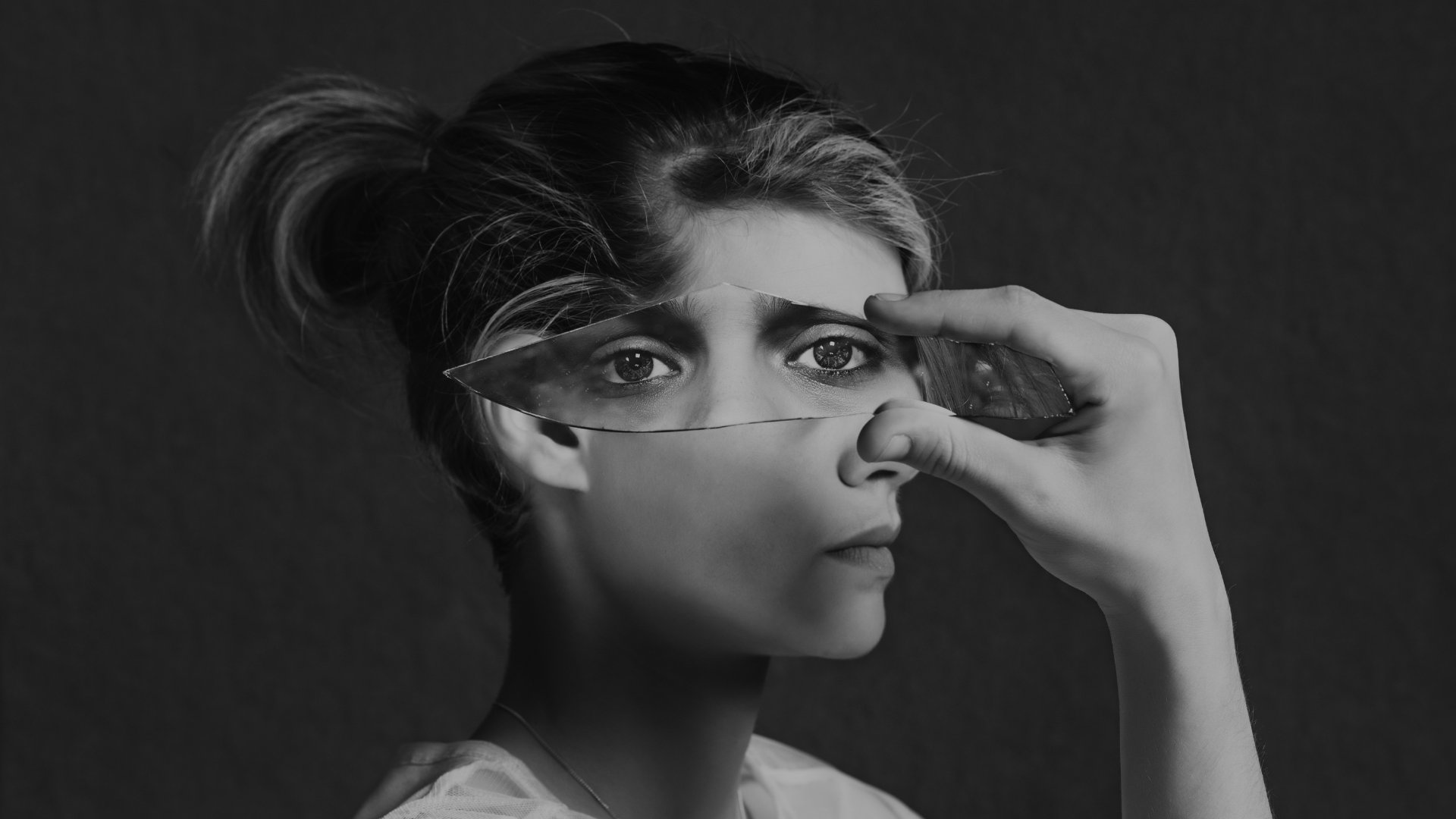 Mulher segurando um pedaço de vidro sobre o rosto, refletindo os olhos