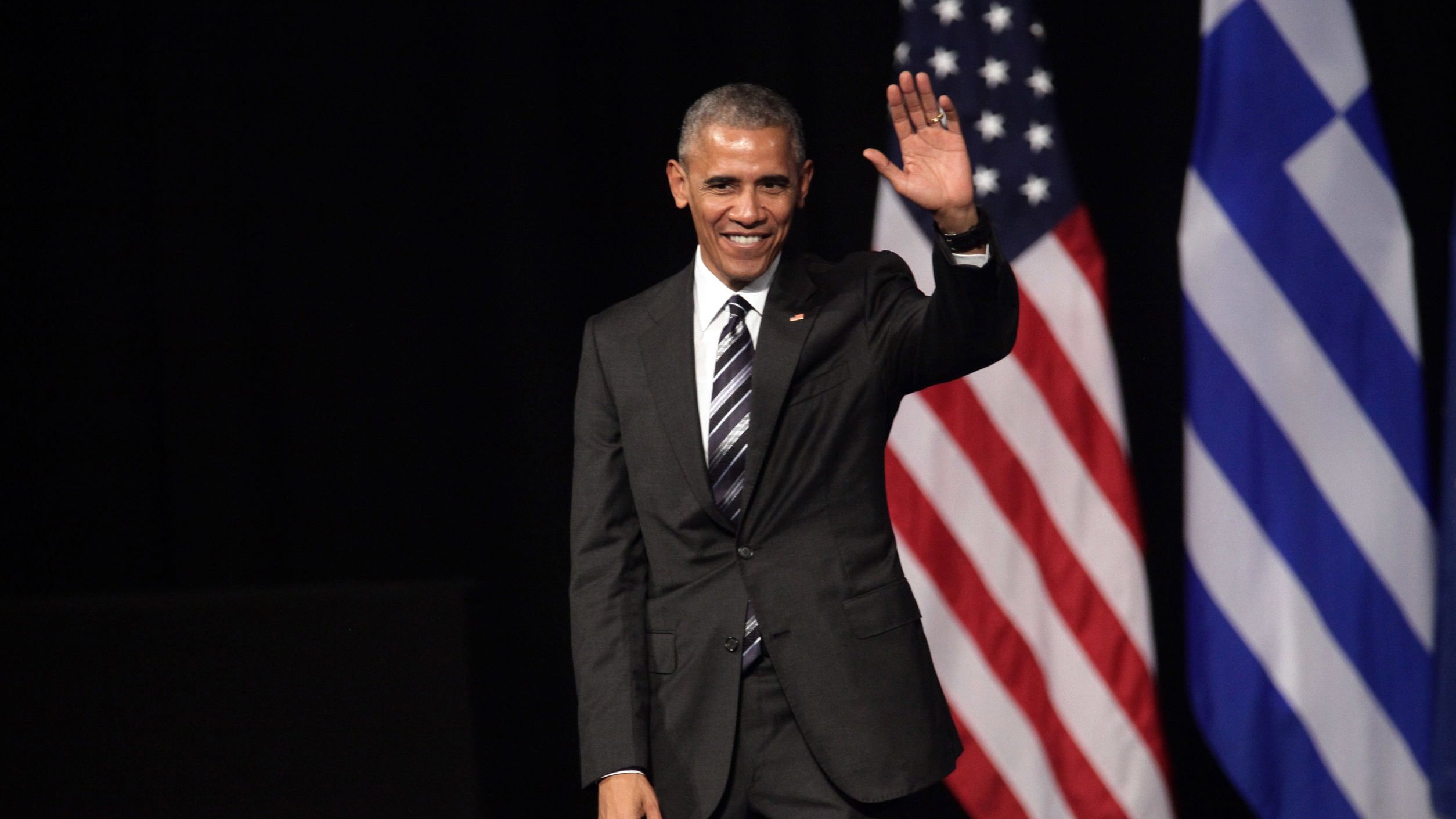 Barack Obama acenando ao lado da bandeira dos Estados Unidos