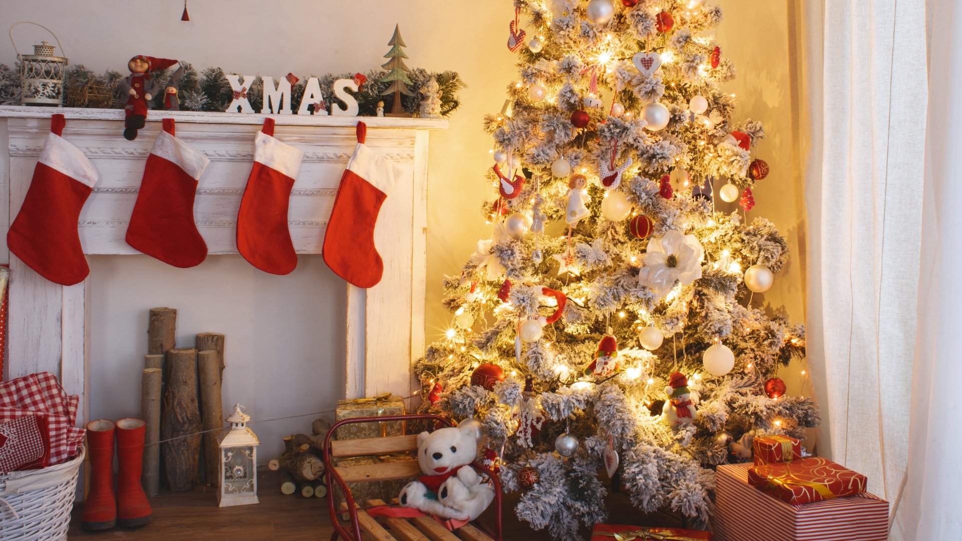 Árvore de natal iluminada com presentes de natal embaixo e meias penduradas na lareira