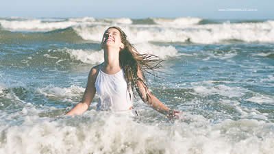 Mulher sorrindo entre as ondas do mar.