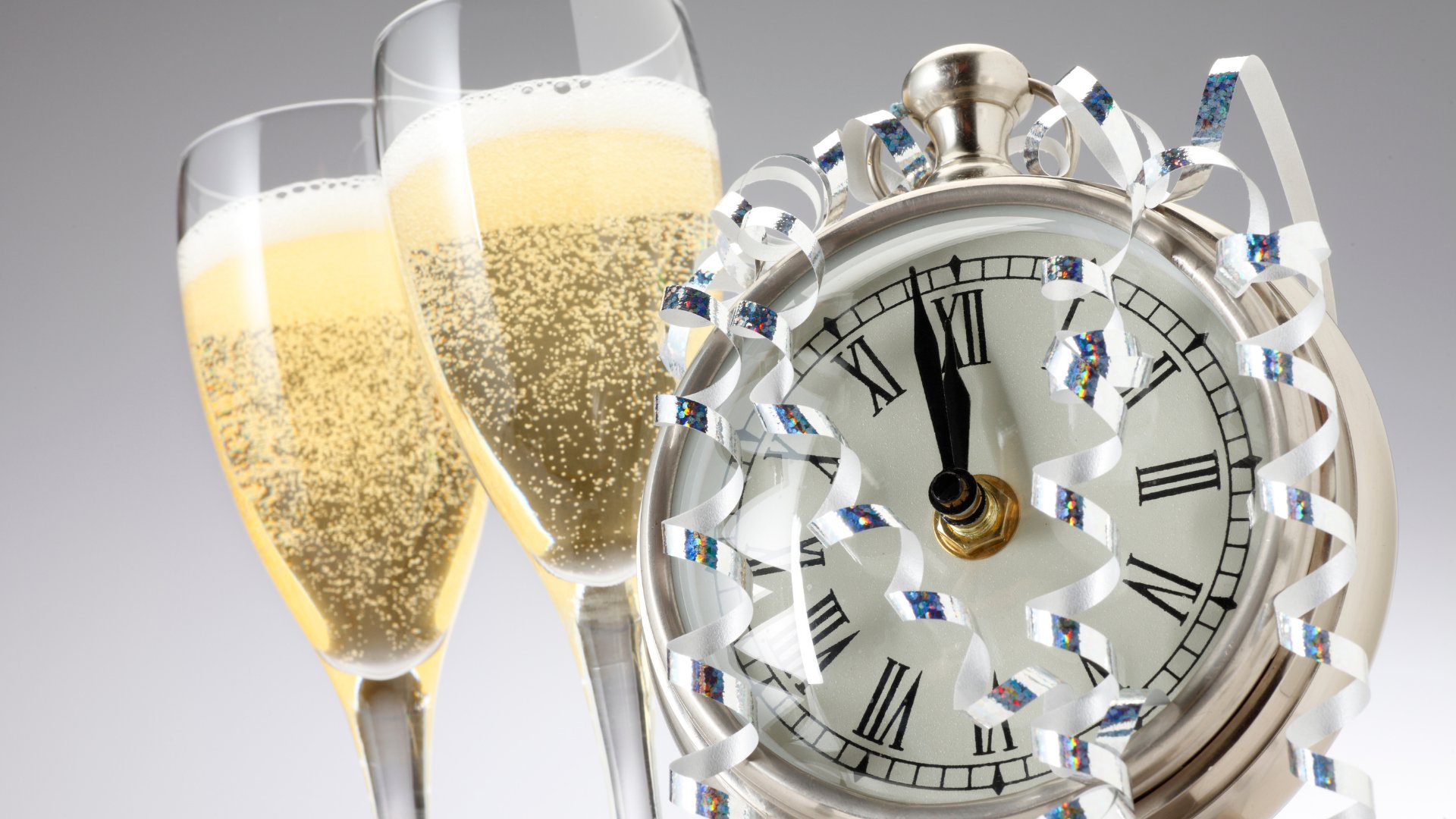 Relógio marcando meia noite com fitas prateadas e duas taças de champagne