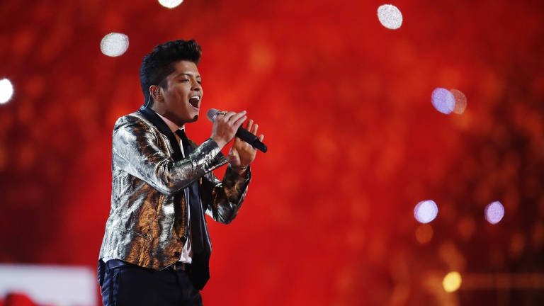 Julio Cortez/Associated Press - Folha Bruno Mars se apresentando em show, com fundo vermelho.