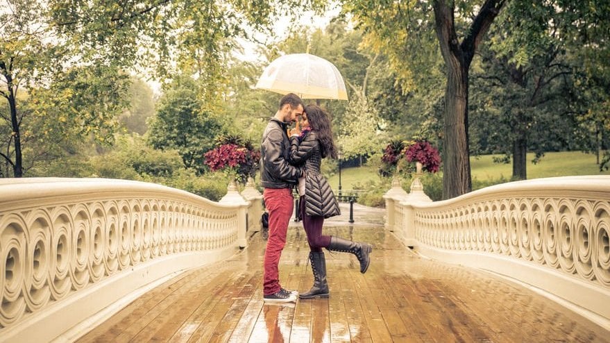 Casal se beijando debaixo do guarda-chuva no parque.