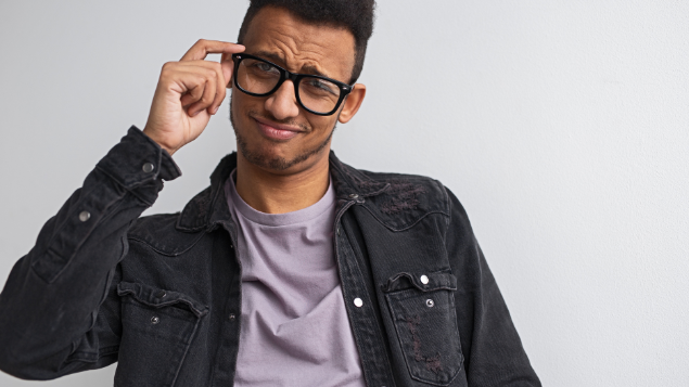 Homem com cara de arrogância e mexendo nas lentes do óculos