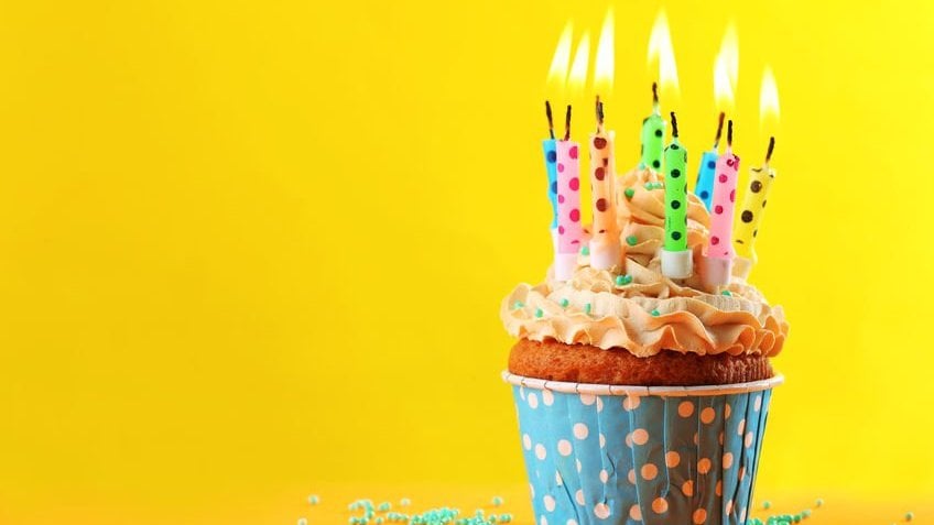 Cupcake colorido com várias velinhas de aniversário acesas em um fundo amarelo