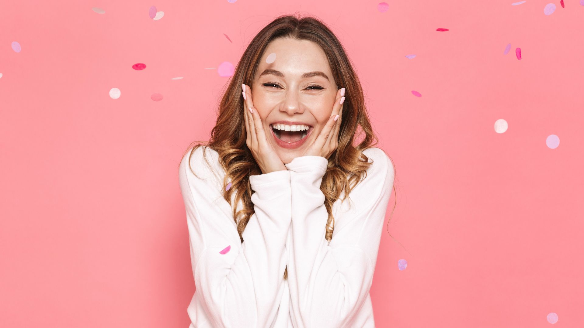 Imagem de uma mulher sorrindo em um fundo rosa e confetes caindo sobre elas