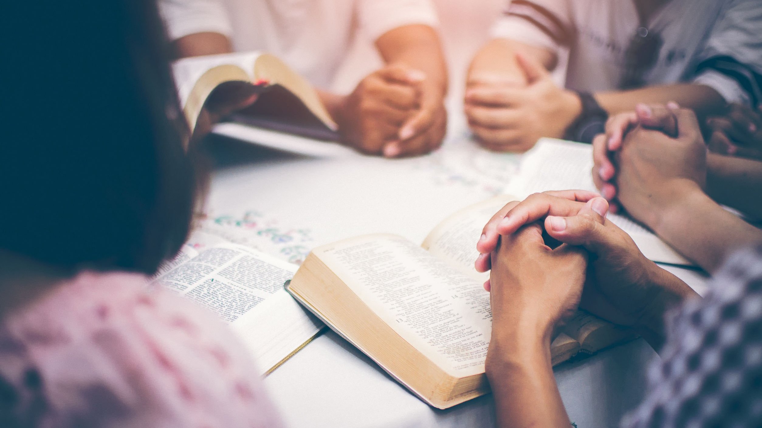 Pessoas rezando com a bíblia em volta de uma mesa