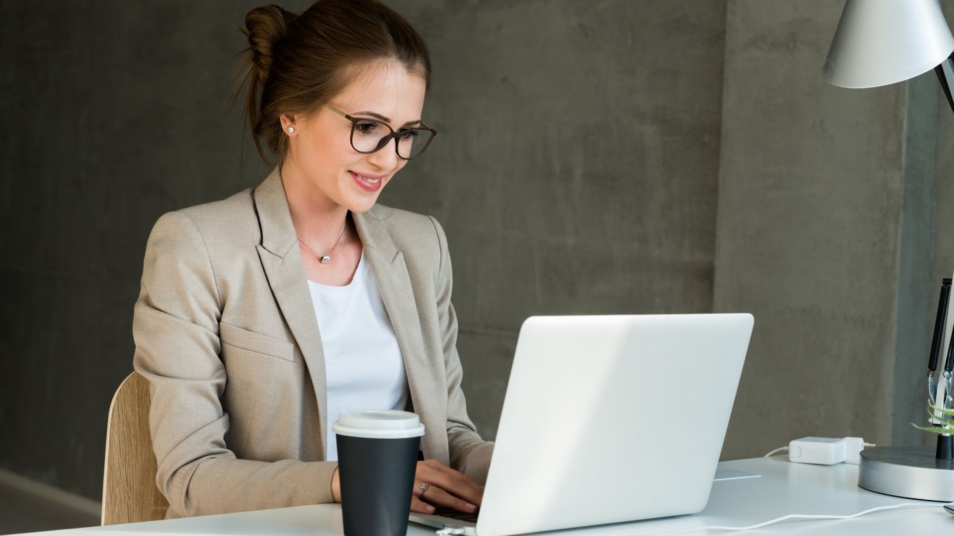 Imagem de uma mulher de óculos sentada na frente do computador no escritório e sorrindo