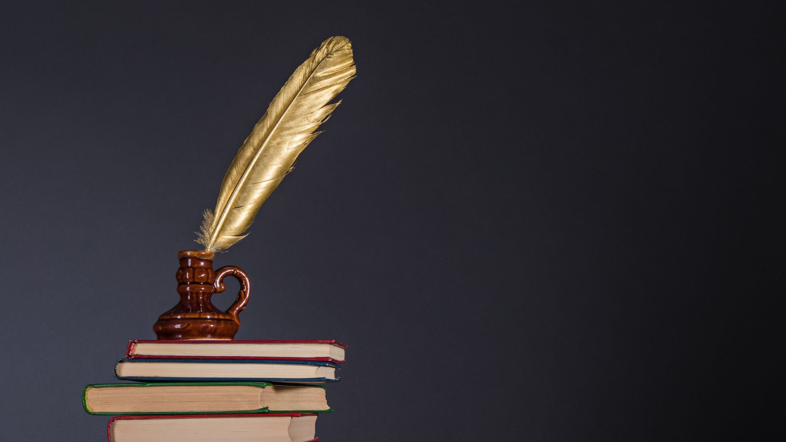 Tinteiro com uma caneta de pena dourada sobre pilha de livros