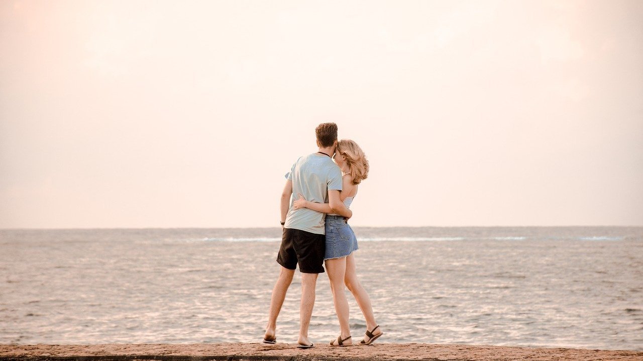 Homem e mulher abraçados de frente para o mar.