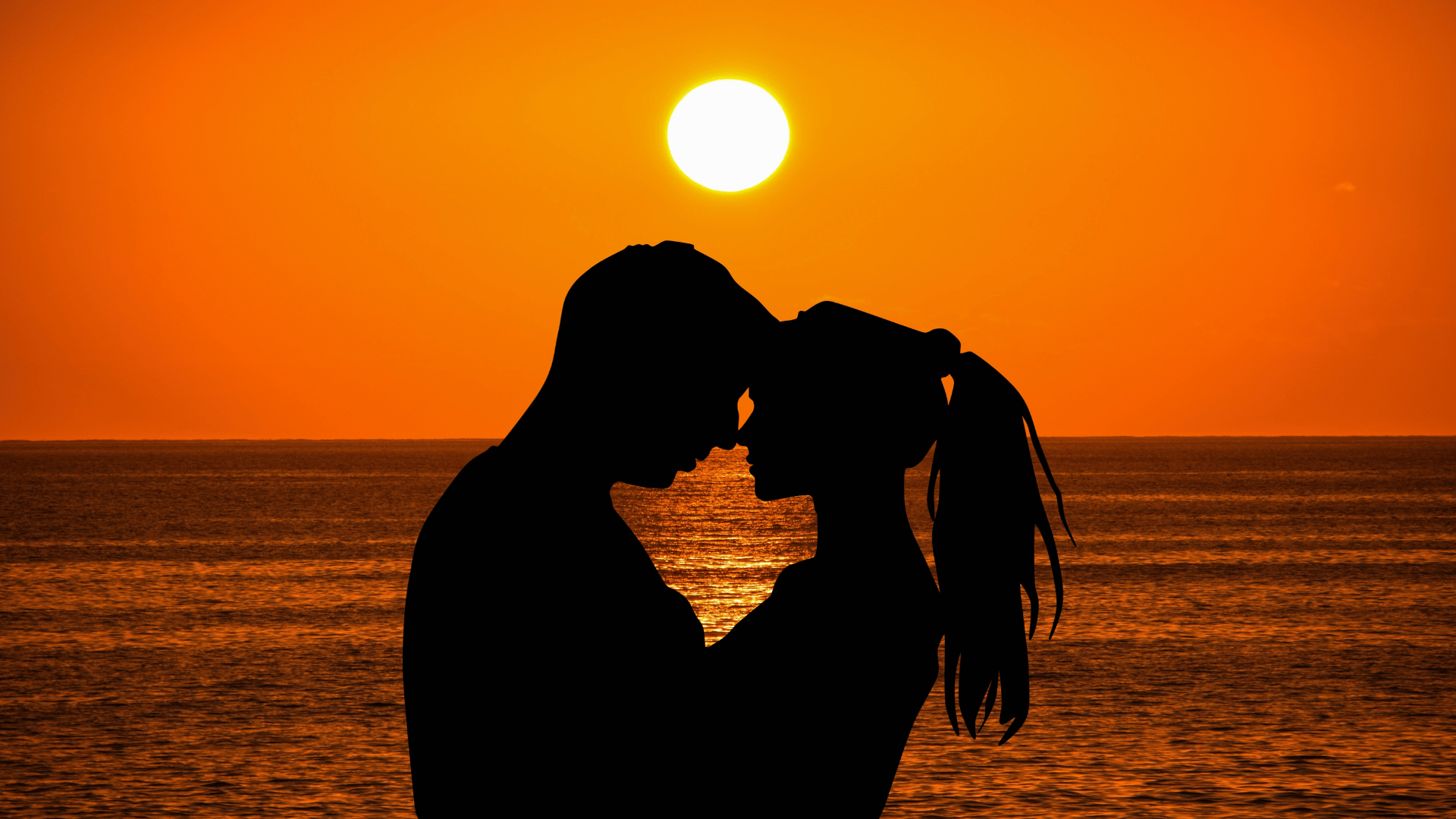 Casal abraçado olhando um para o outro. Ao fundo, o mar e um lindo pôr do sol.