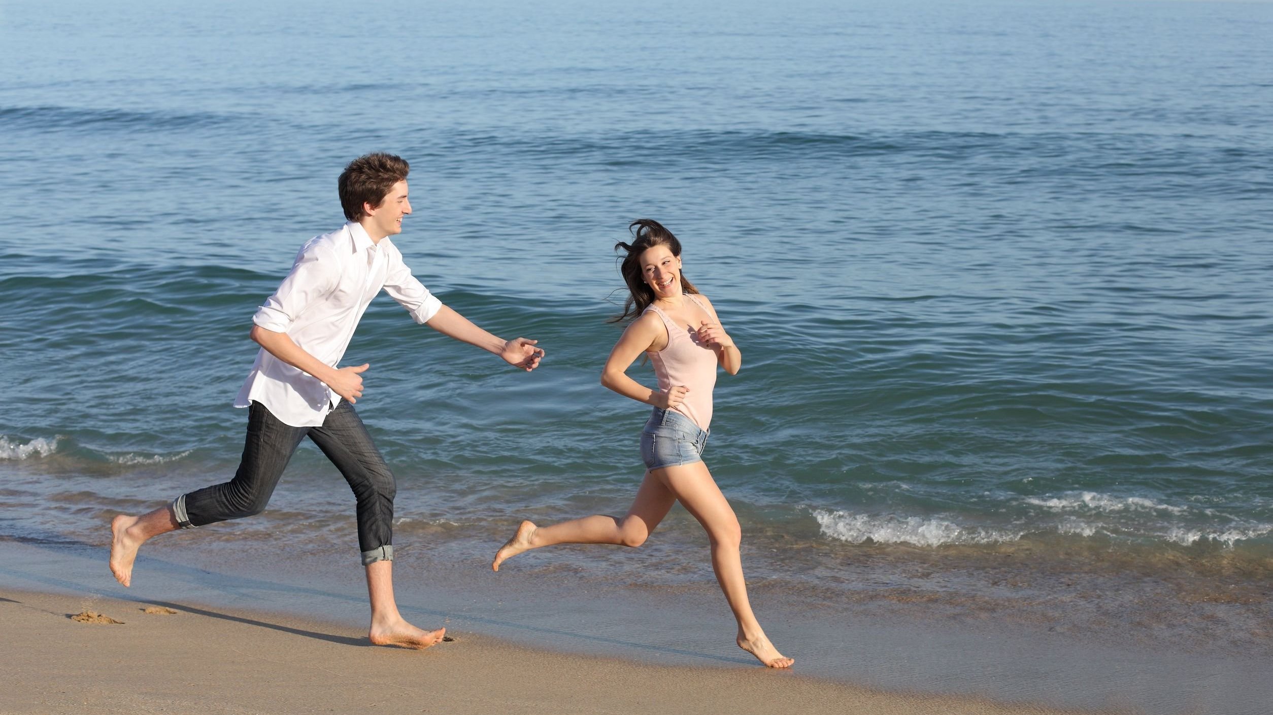 Homem correndo atrás de mulher em praia.