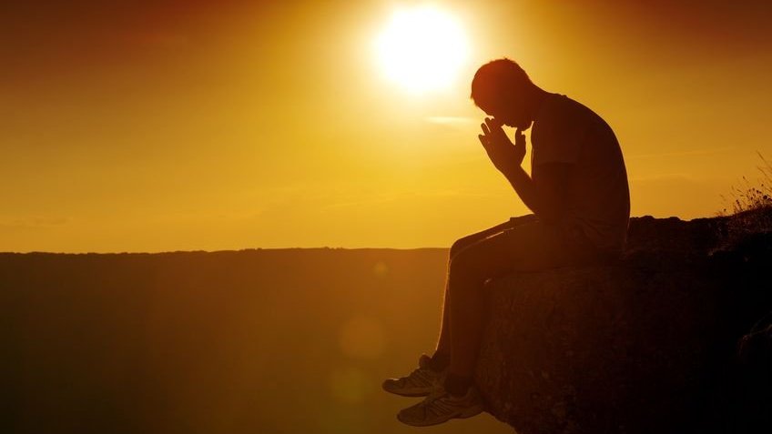 Homem rezando no pico de uma montanha durante o pôr do sol