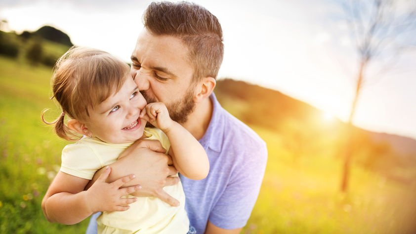 Pai abraçando e beijando a filha pequena.