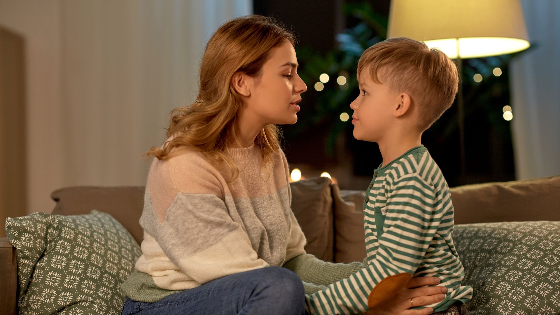 Imagem de mãe e filho conversando e sentados em um sofá de cor bege.