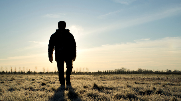 Homem andando em um campo enquanto o sol nasce