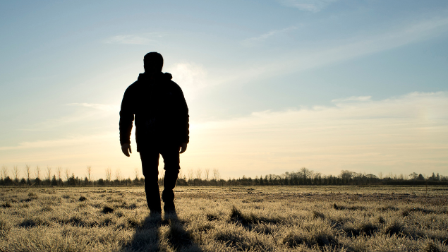 rocksunderwater / Getty Images Signature Homem andando em um campo enquanto o sol nasce
