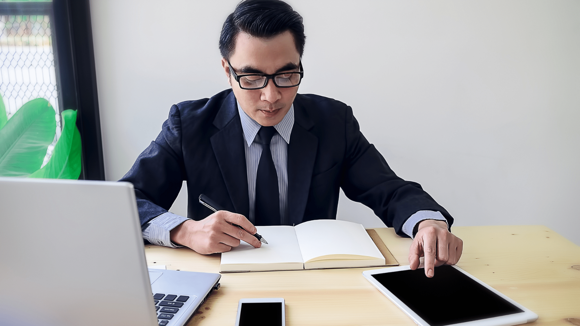 Imagem de um empresário em seu escritório com um Tablet e fazendo anotações.
