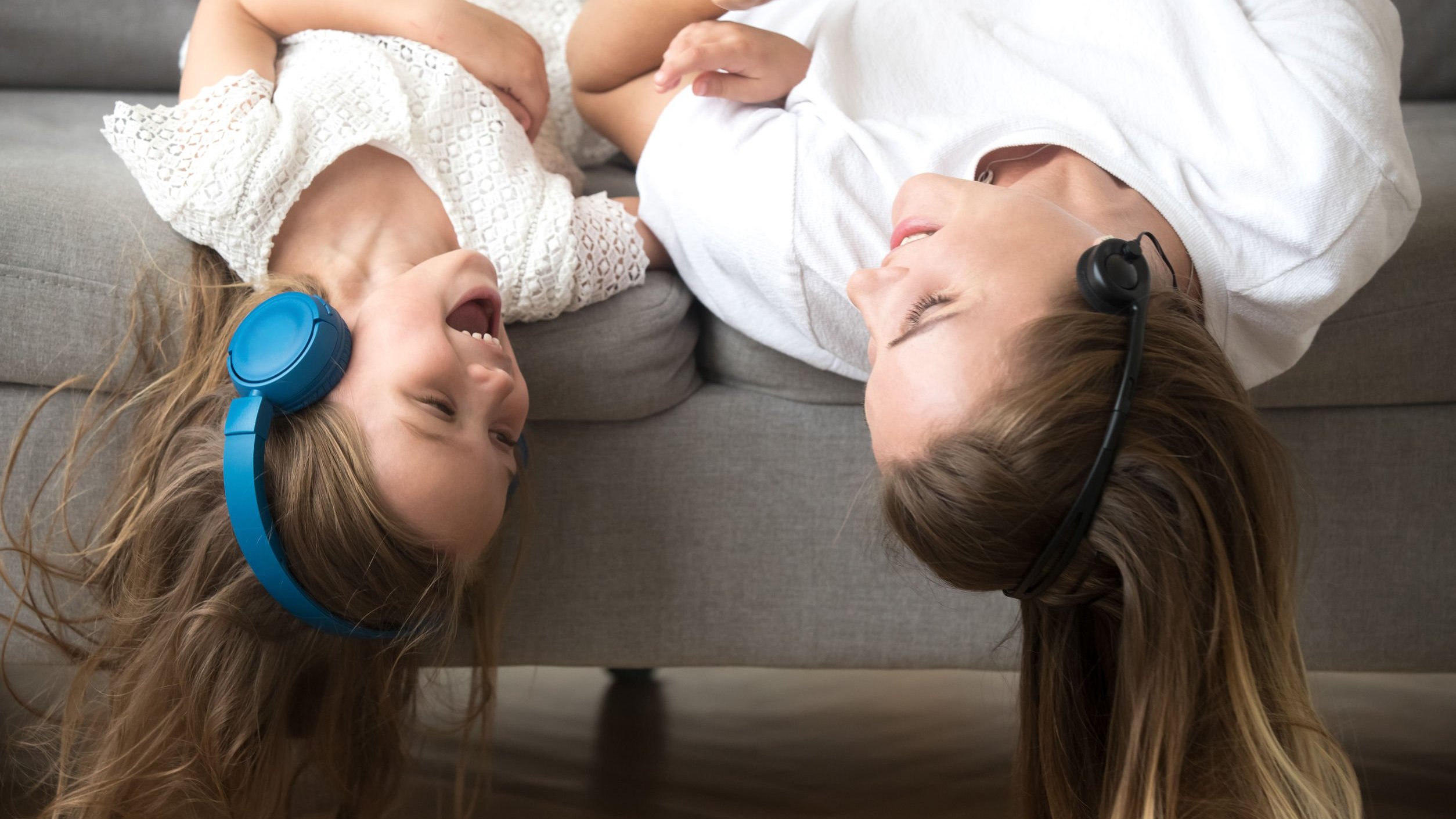 Amigas ouvindo música com fones de ouvido deitadas no sofá de cabeça para baixo