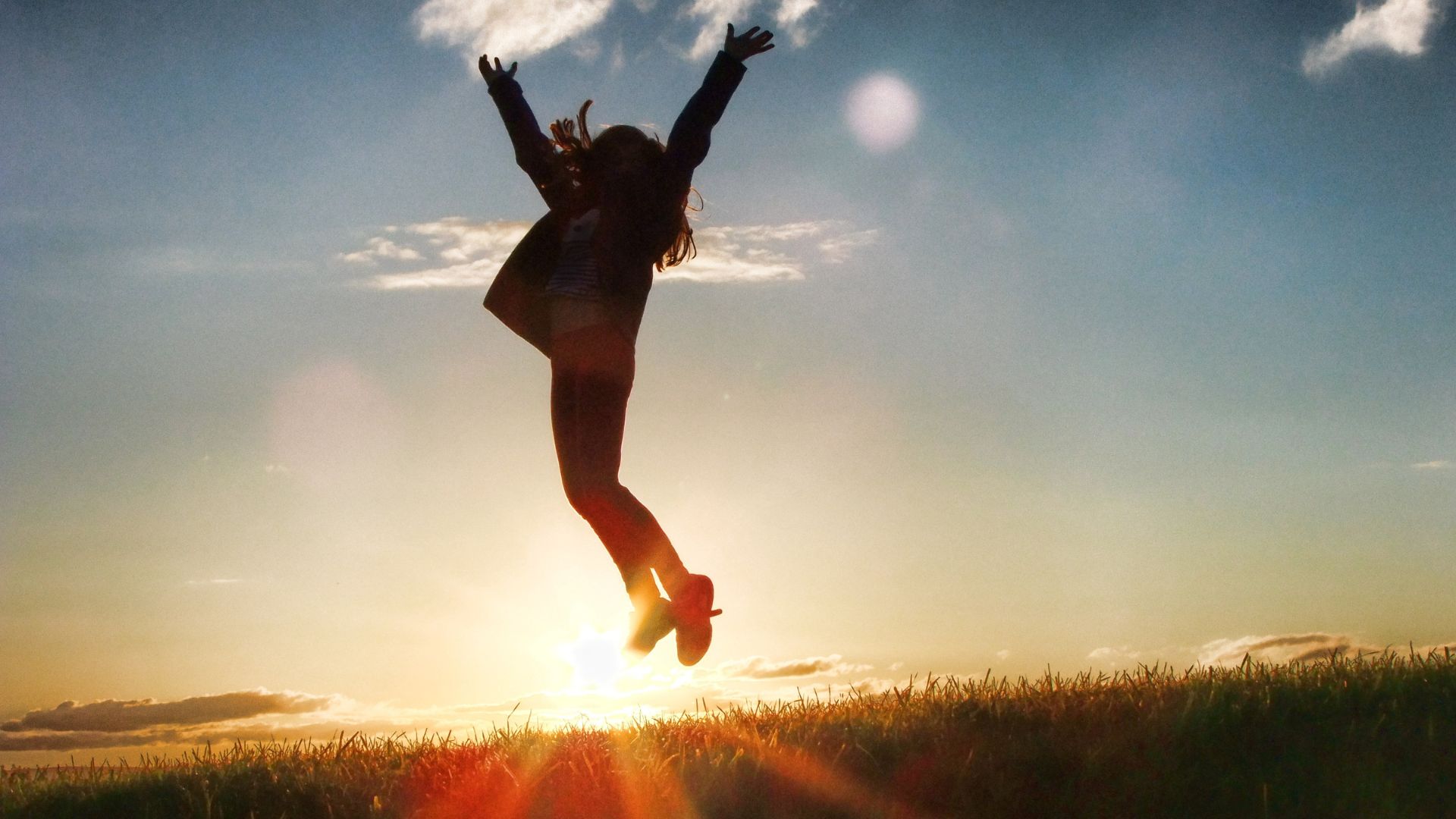 Imagem de uma moça saltando com o braços para cima. Ao fundo, o céu azul e raios de sol.