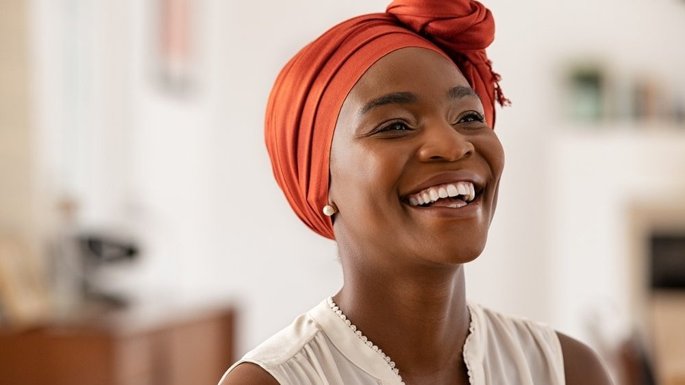 Mulher negra de lenço vermelho na cabeça sorrindo.