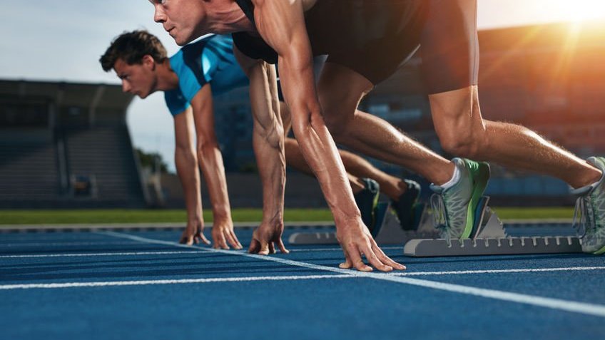 Dois jovens atletas na posição inicial, prontos para iniciar uma corrida.