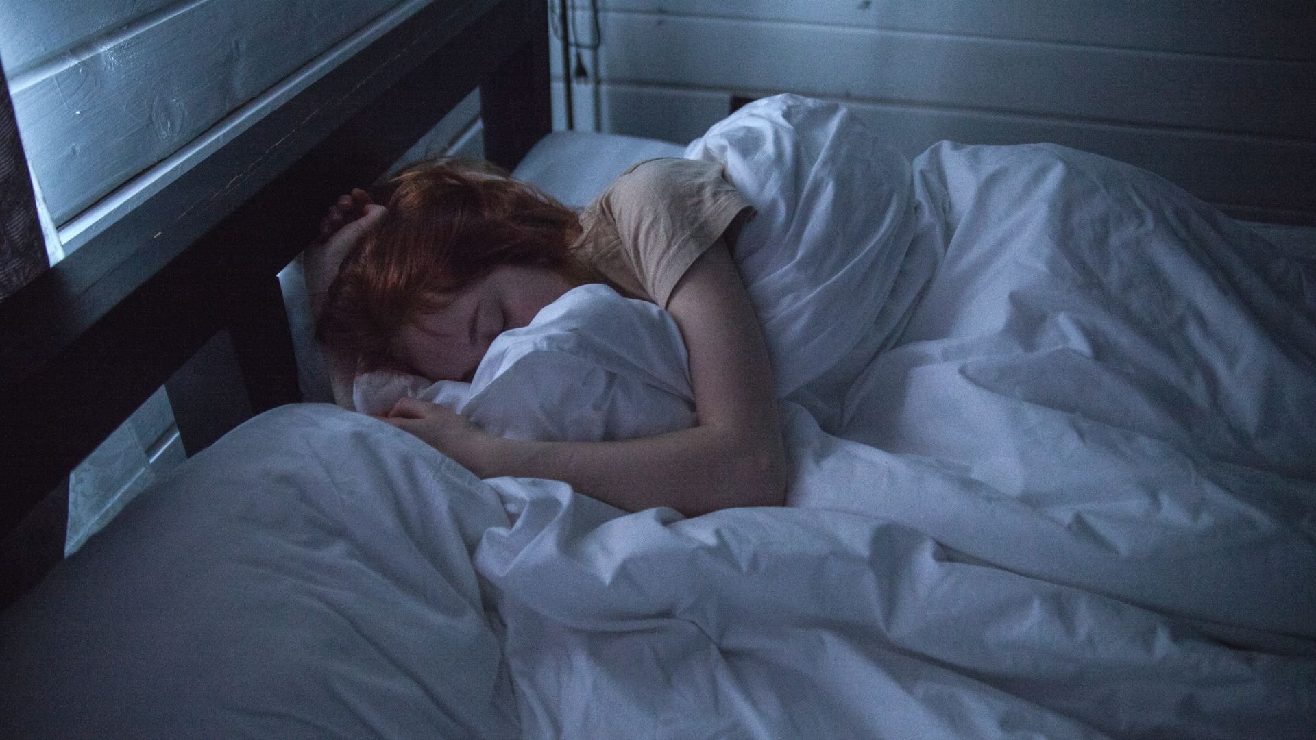 Imagem de uma mulher deitada na cama dormindo envolta em um edredom branco