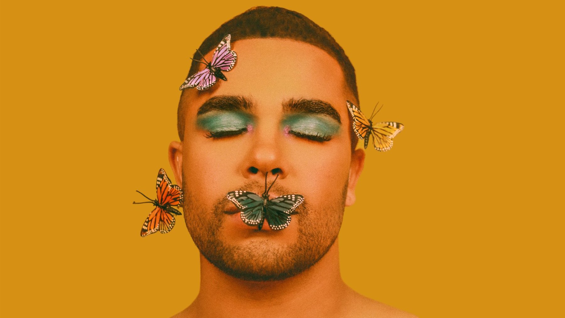 Homem branco com maquiagem azul e borboletas no rosto.