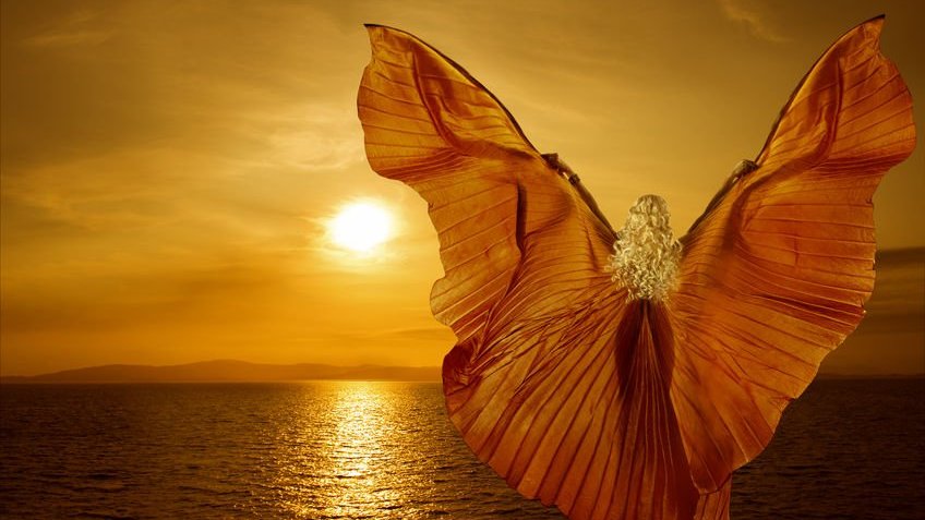 Mulher com asas olhando para pôr do Sol