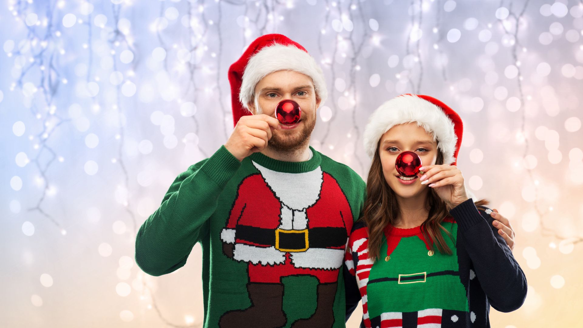 Imagem de fundo prateado. Em destaque, um casal usa um boné de Natal e um suéter verde de manga longa, com a foto do papai noel estampada.