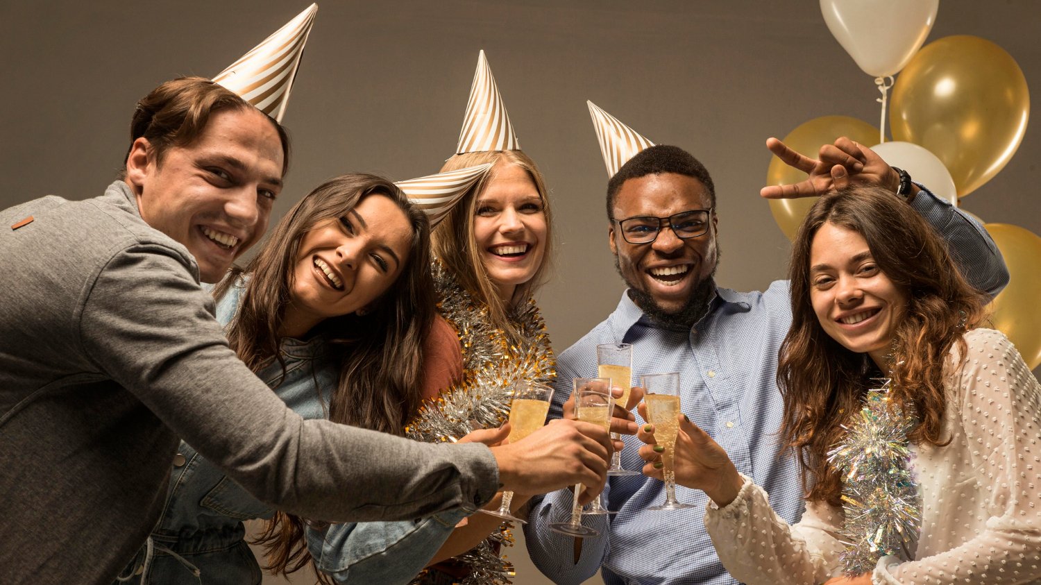 Amigos comemorando a chegada do ano novo, usando chapéus de festa e segurando taças de bebidas.