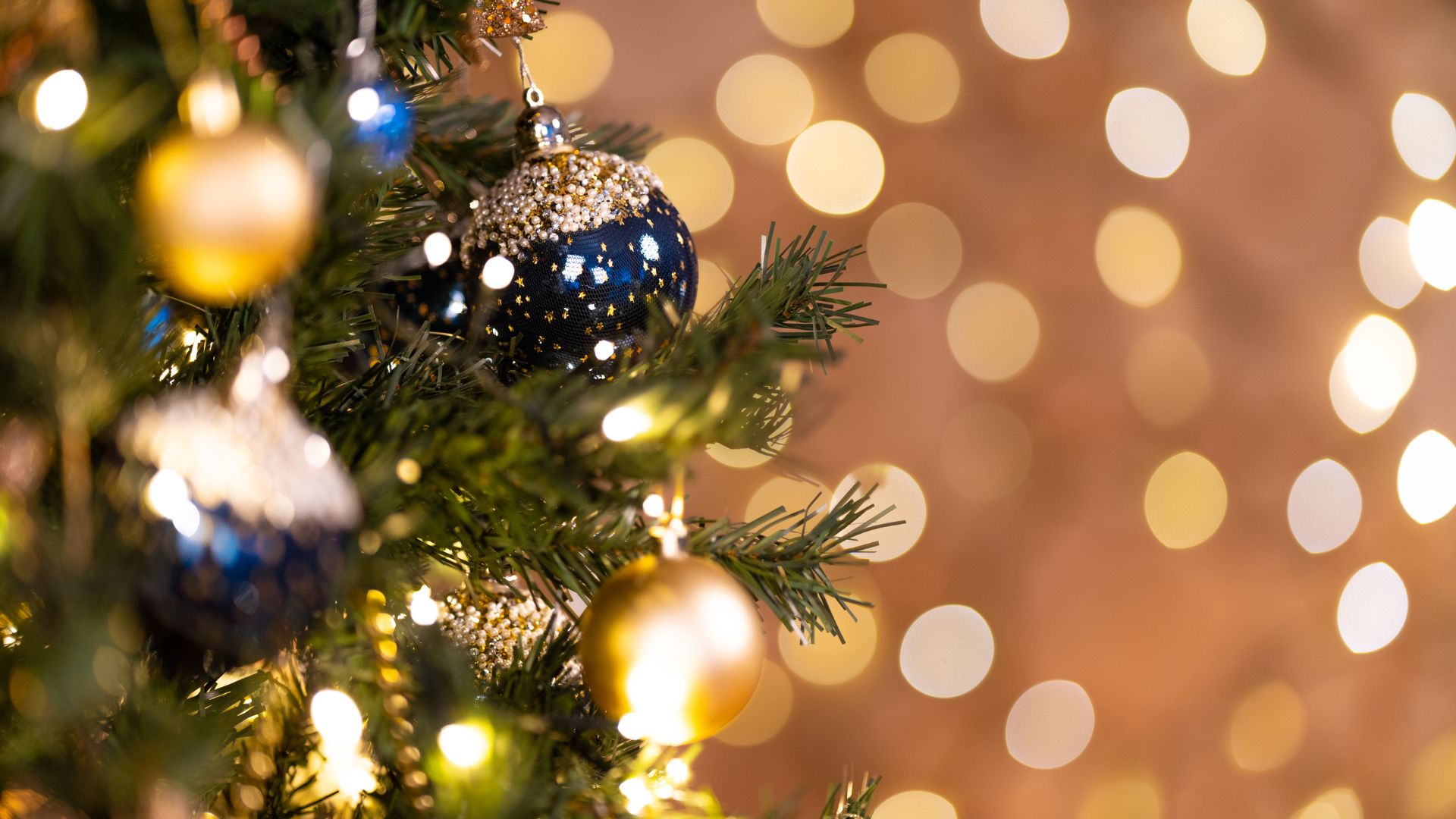 Imagem de fundo dourado. Do lado esquerdo da tela, um galho de árvore de natal decorado com bolas azuis e douradas.