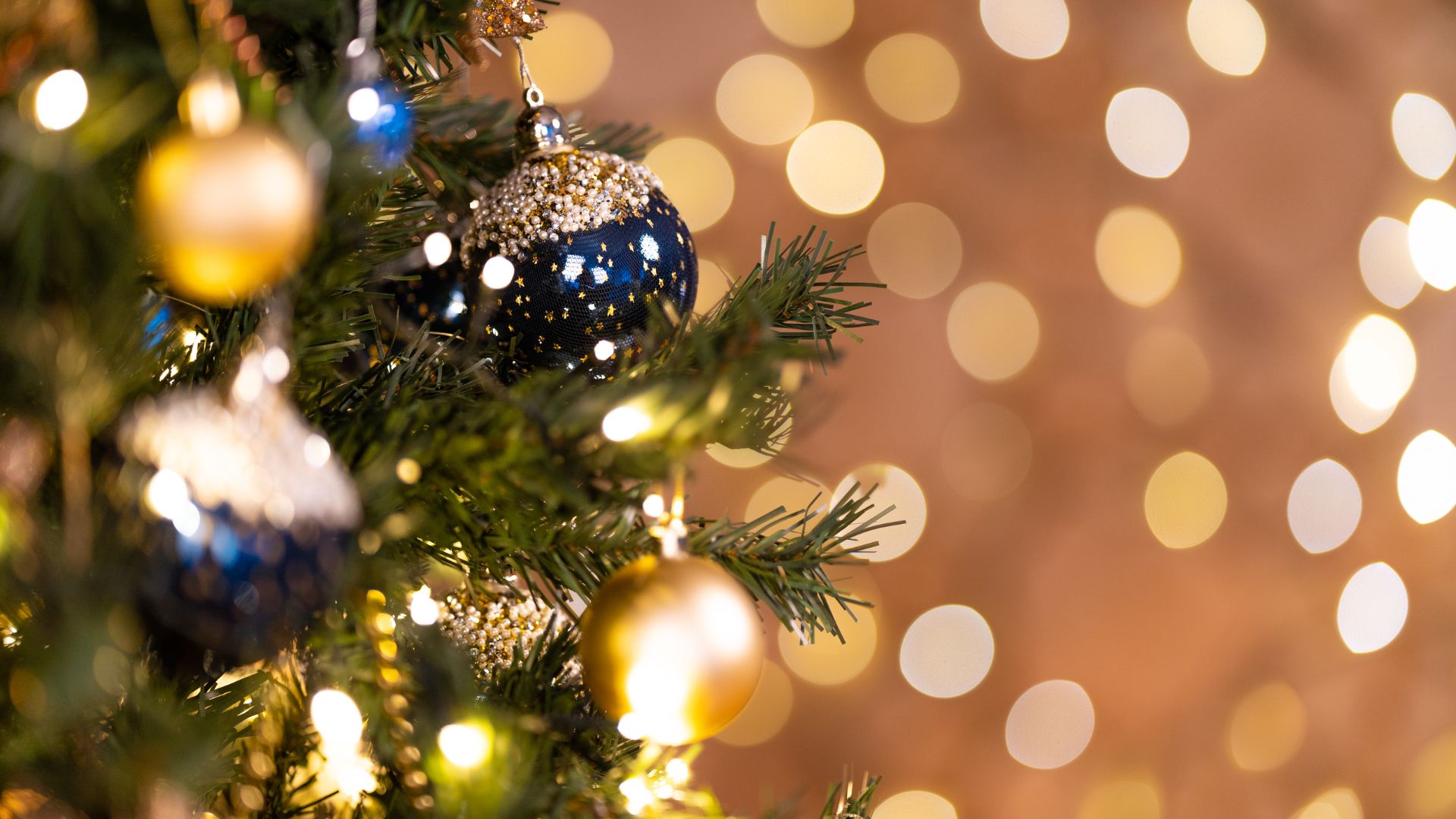 Hunt on Photos Studio de Pexels para o Canva Imagem de fundo dourado. Do lado esquerdo da tela, um galho de árvore de natal decorado com bolas azuis e douradas.